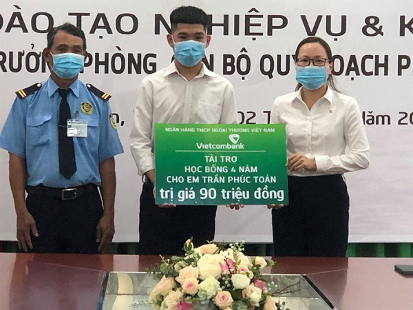 Bà Nghiêm Thị Hoa – Phó Giám đốc Vietcombank Long An trao bảng tượng trưng số tiền học bổng cho em Trần Phúc Toàn và cha