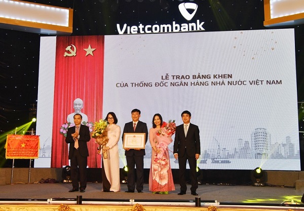 Ông Nguyễn Đồng Tiến - Ủy viên Ban cán sự  Đảng, Phó Thống đốc NHNN (ngoài cùng bên trái) trao Bằng khen của Thống đốc NHNN và ông Nghiêm Xuân Thành – Bí thư Đảng ủy, Chủ tịch HĐQT Vietcombank (ngoài cùng bên phải) tặng hoa cho ông Lê Ngọc Thái – Giám đốc