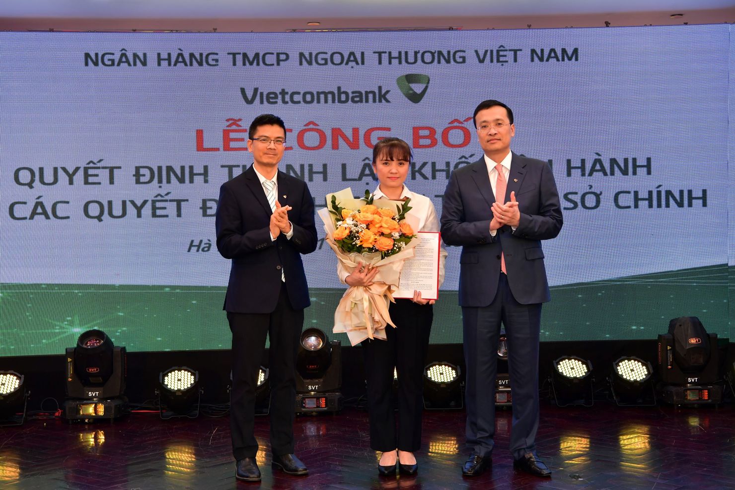 Ông Phạm Quang Dũng - Chủ tịch HĐQT (bên phải) trao quyết định và ông Trần Thanh Nam - Giám đốc Khối Vận hành (bên trái) tặng hoa chúc mừng bà Thái Thị Thu Hằng - tân Phó trưởng phòng phụ trách Phòng Quản lý chất lượng - Trụ sở chính Vietcombank.